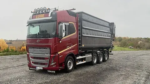 Rød Volvo lastebil med svart tippkasse parkert på grusplass.