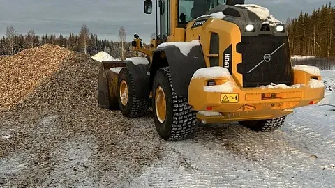 Gul hjullaster fra Volvo laster flis i vinterkledd terreng.